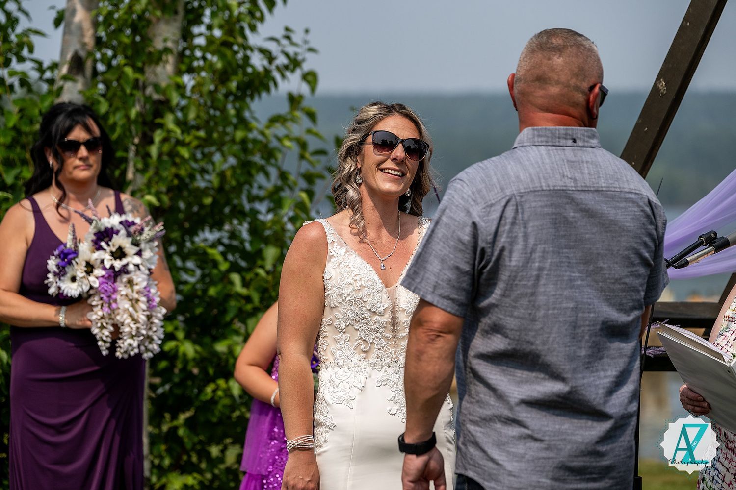 Wedding ceremony guests gathered outdoors with purple and white attire.