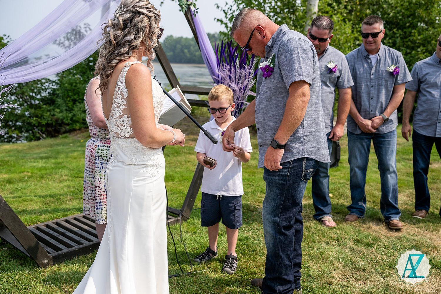 Outdoor wedding ceremony with guests gathered under purple arch decor.