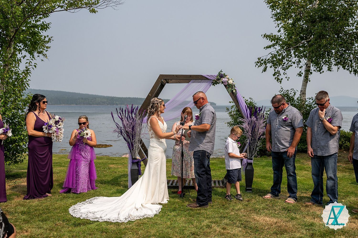 Lakeside wedding ceremony with purple-themed decor and gathered guests.