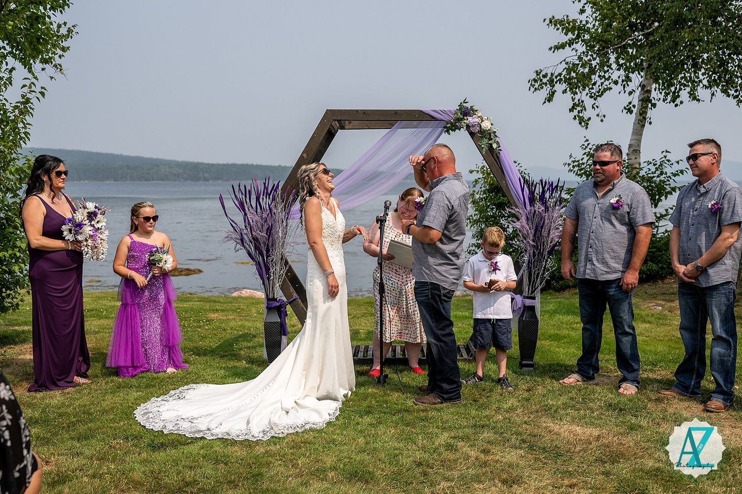 Outdoor wedding processional taking place by a waterfront with white decorative elements.