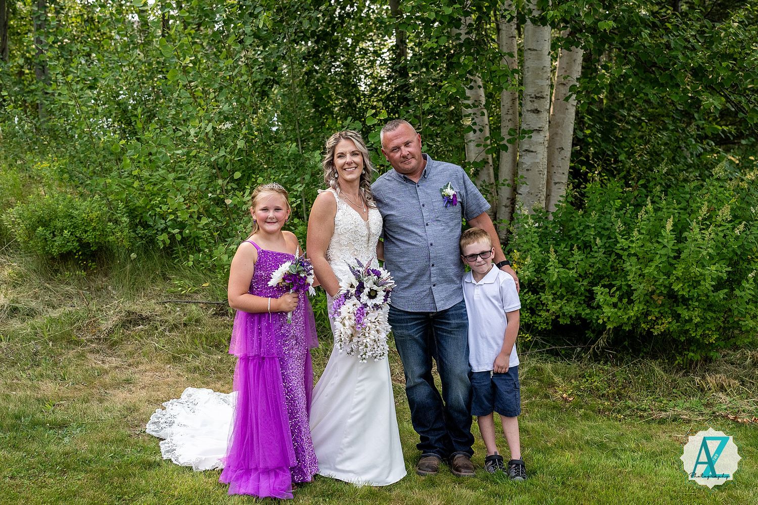 Wedding party stands together outdoors with birch trees and green foliage in the background.