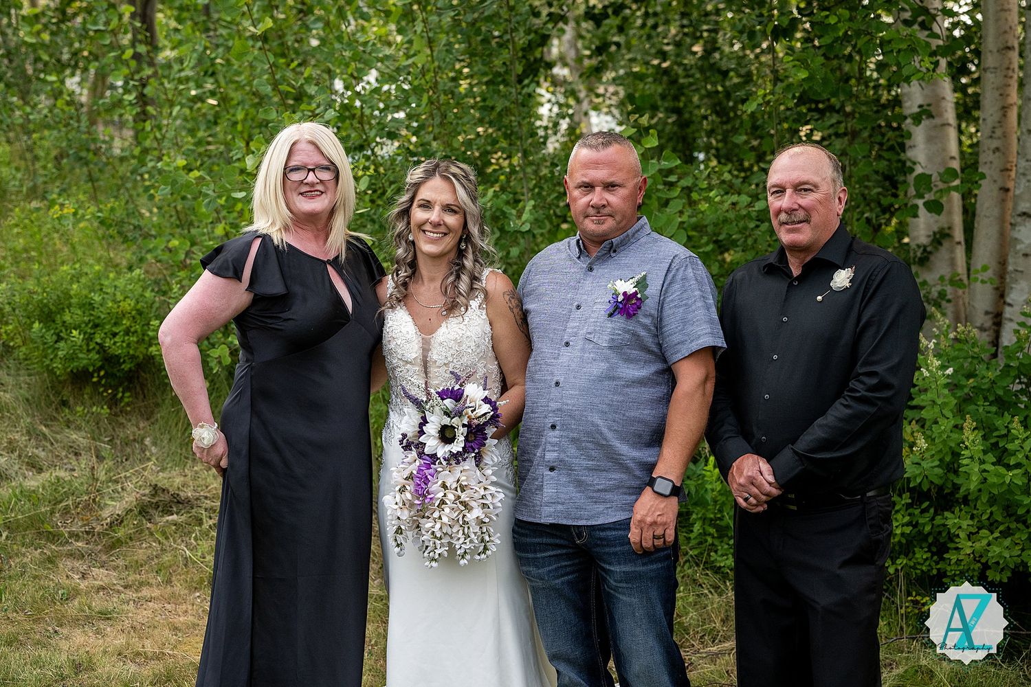 A small group poses together at an outdoor wedding celebration with trees in the background.