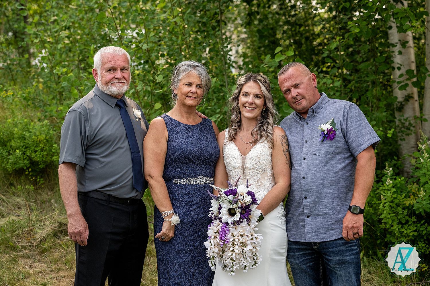 A small wedding group stands together in front of birch trees and greenery on a summer day.