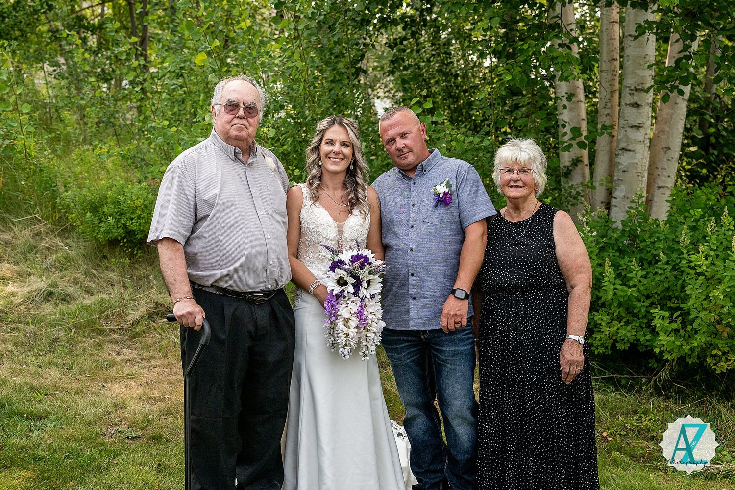 A small group poses together for a formal photo outdoors with aspen trees in the background during summer.