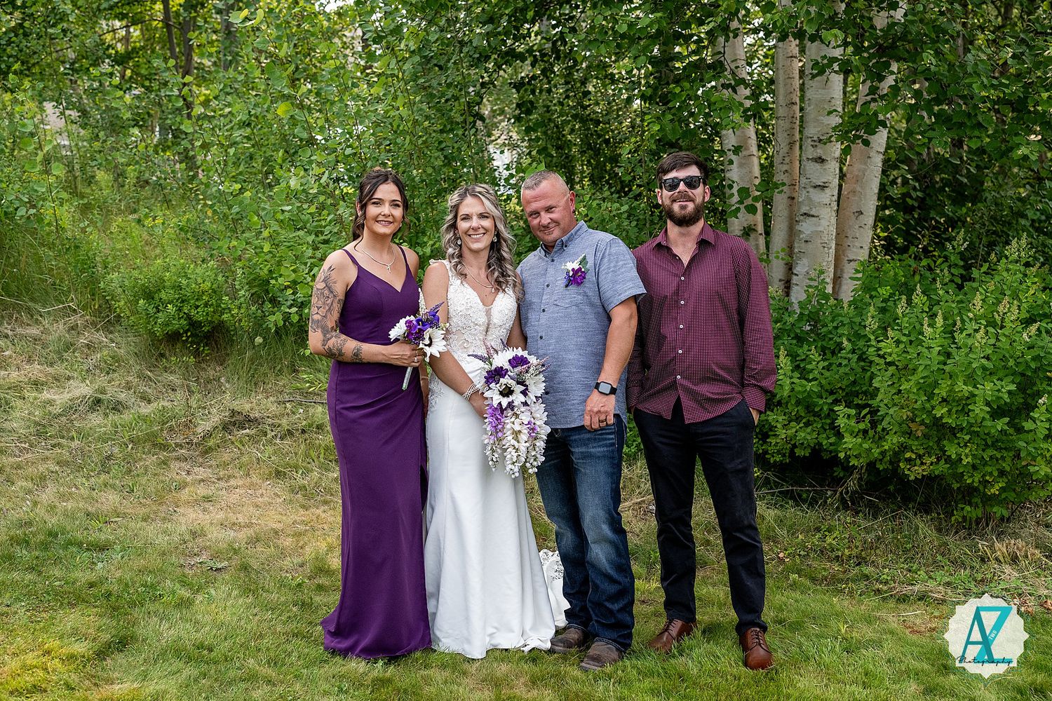 Small wedding group of four people posing together outside with trees and foliage in the background.