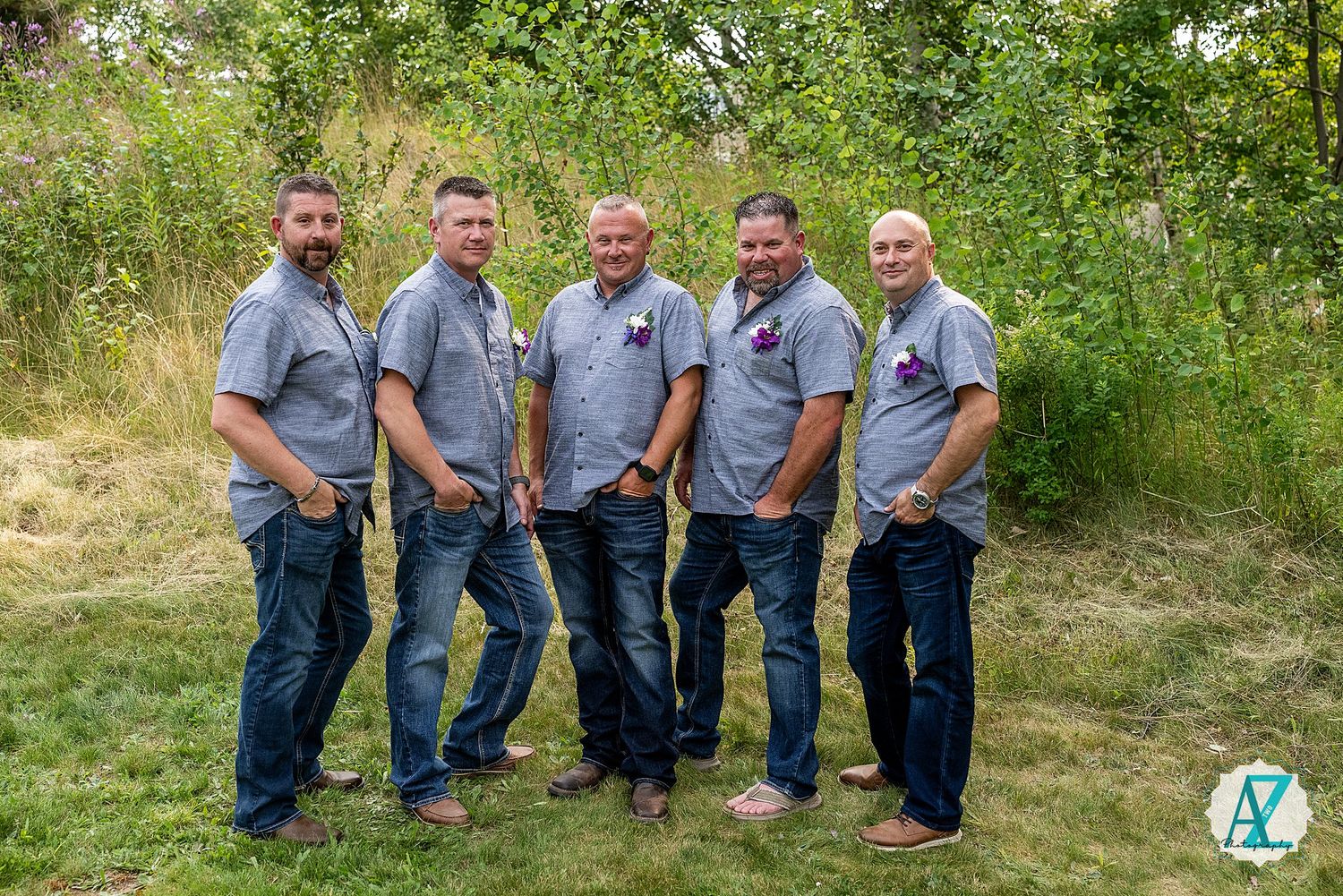 Team of maintenance workers in matching gray polo shirts and jeans pose together outdoors in a garden setting.