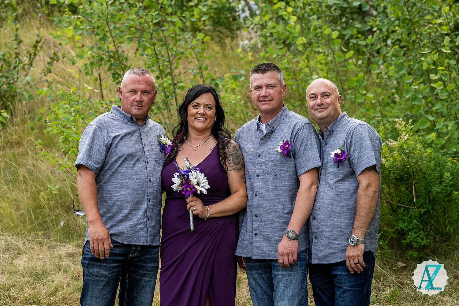 A group of four people wearing gray and purple attire pose together outdoors against a green natural background.