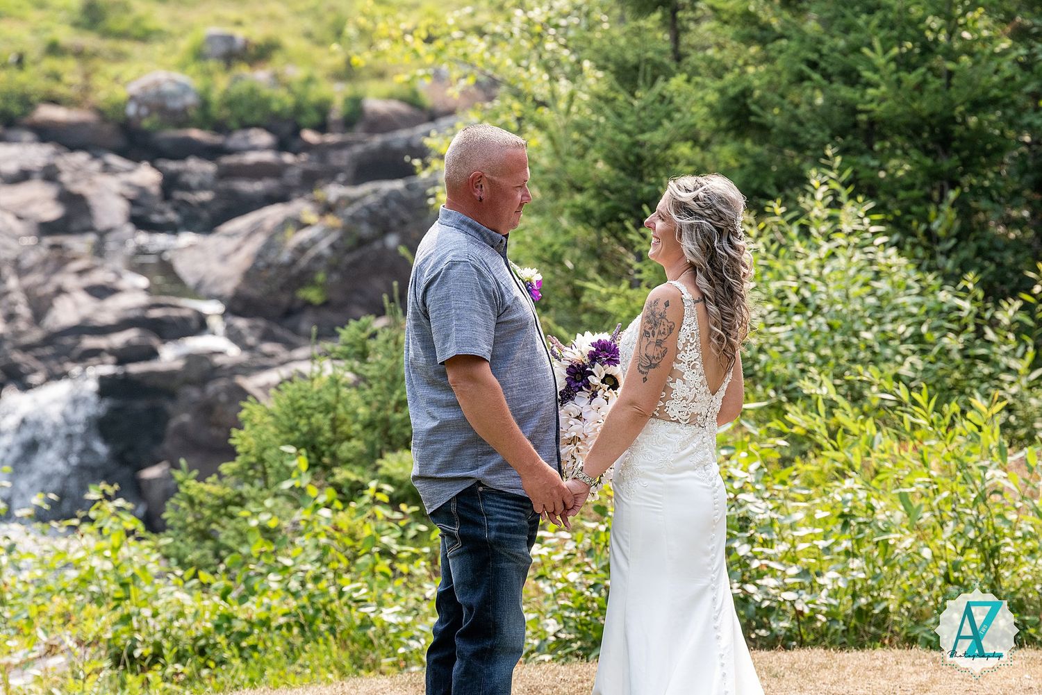 A couple shares a romantic moment outdoors by a cascading waterfall surrounded by lush greenery.