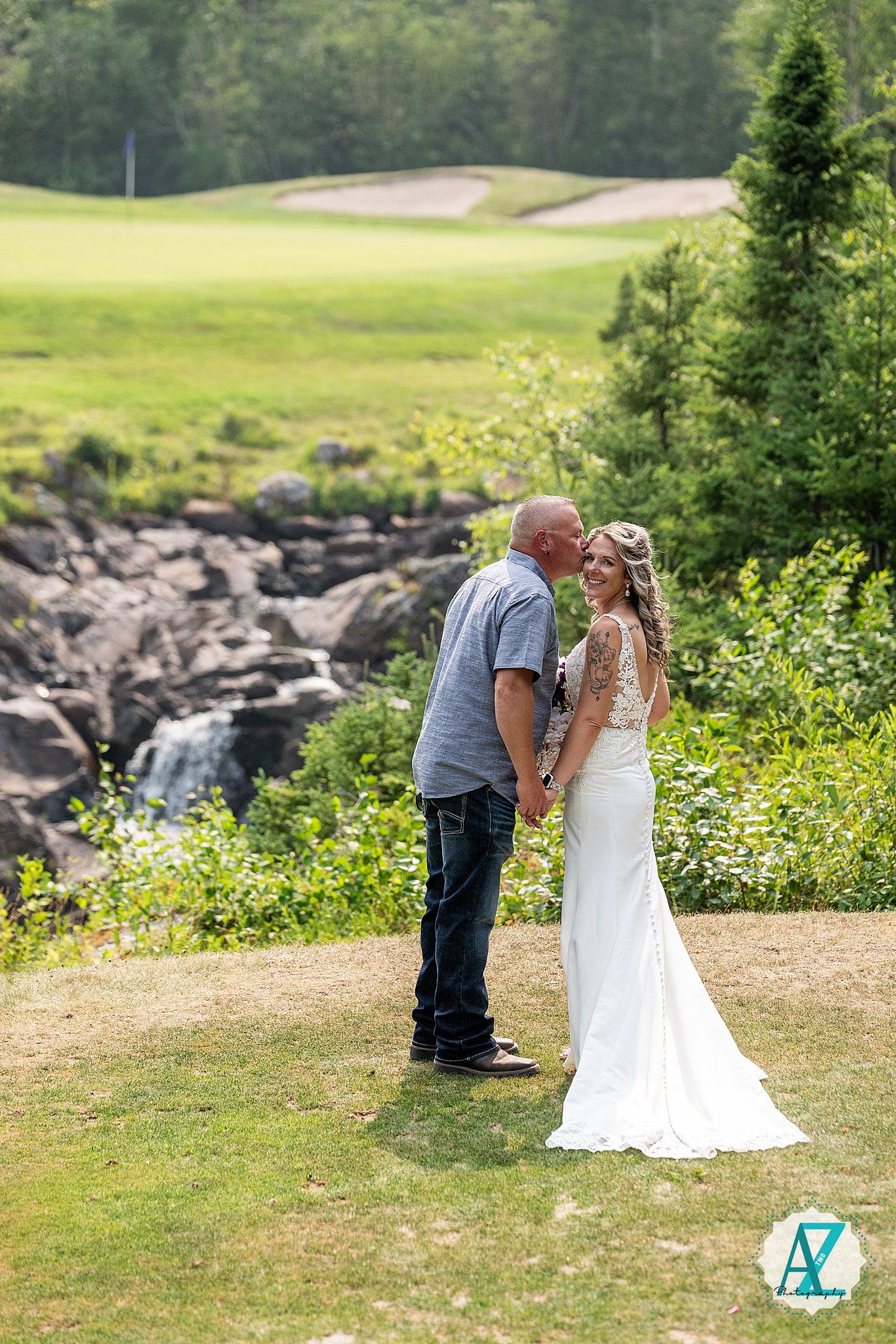 A romantic moment captured at an outdoor wedding venue with lush greenery and rocky landscape in the background.