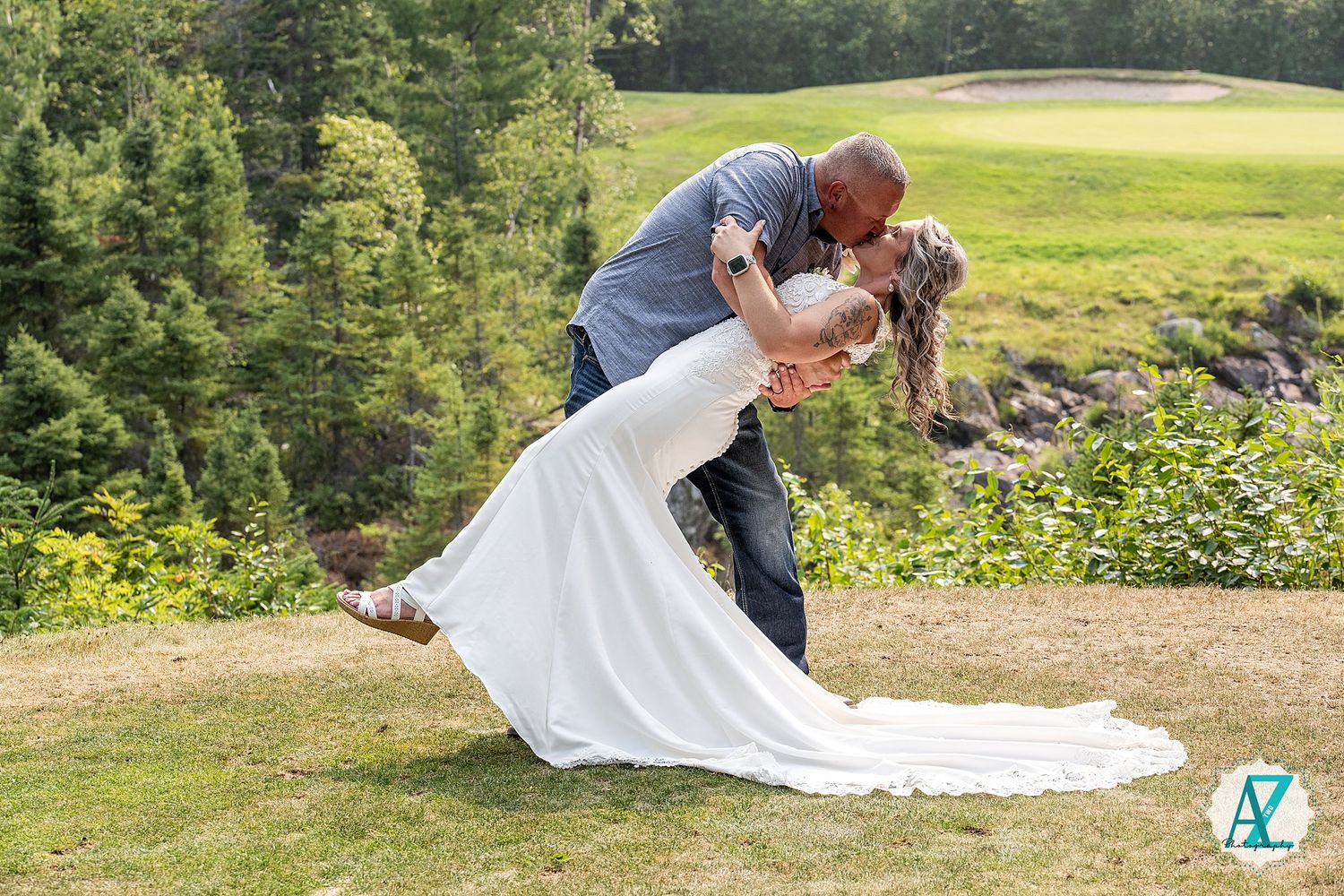 A couple shares a romantic dip kiss on a golf course with a flowing white wedding dress trailing on the ground.