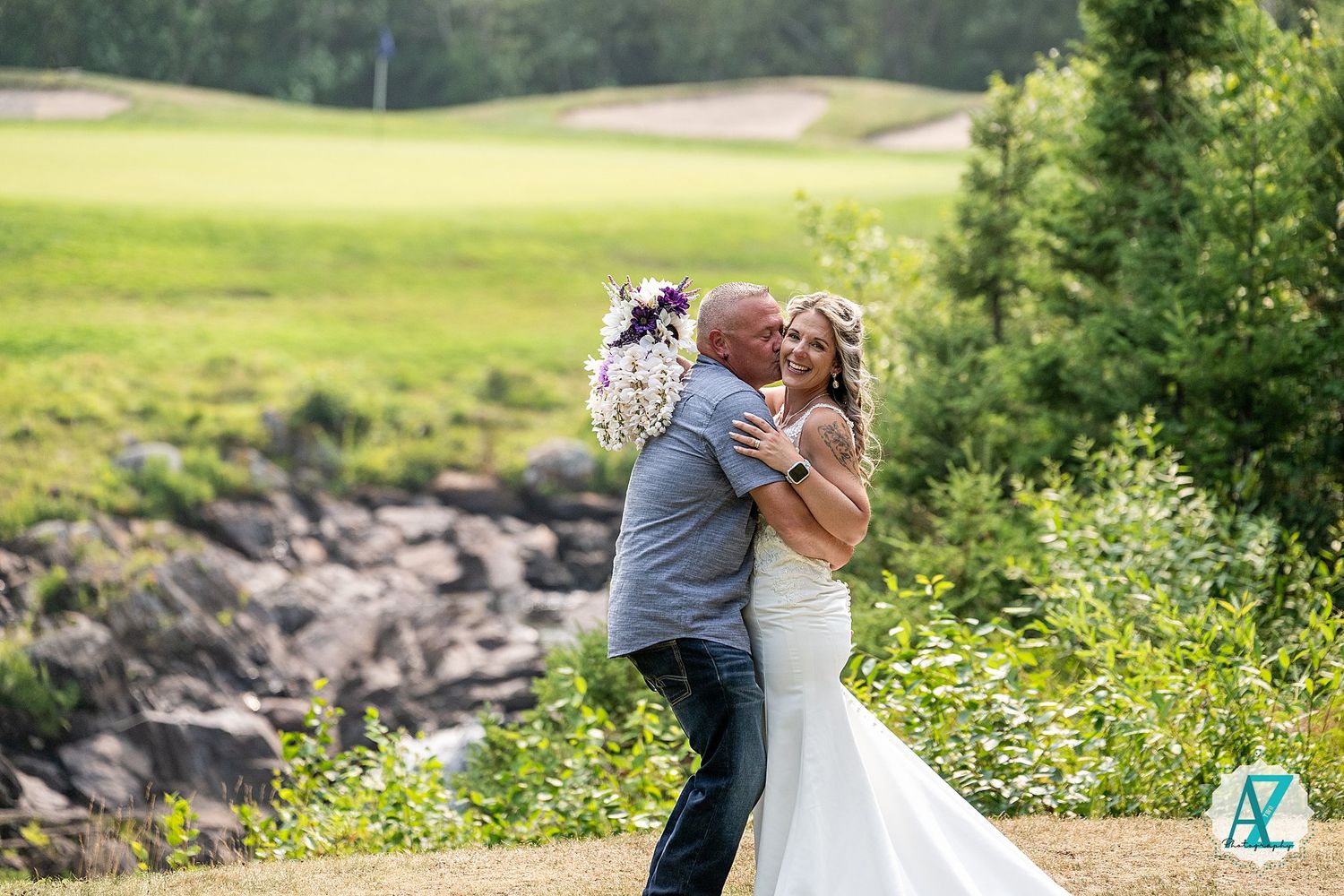 A happy couple shares a romantic kiss on a hilltop surrounded by lush greenery and wildflowers on their wedding day.
