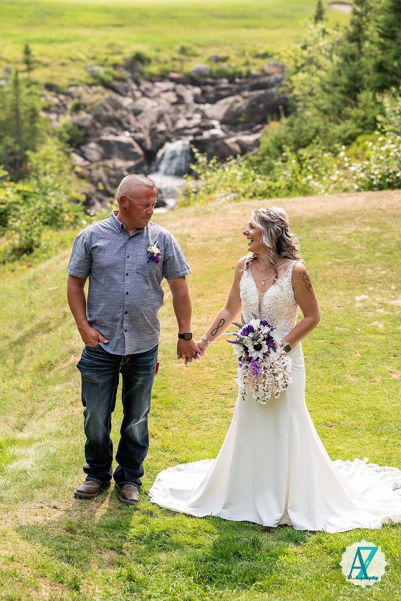 A couple enjoys their wedding day amongst a scenic mountain meadow with wildflowers and a waterfall in the background.