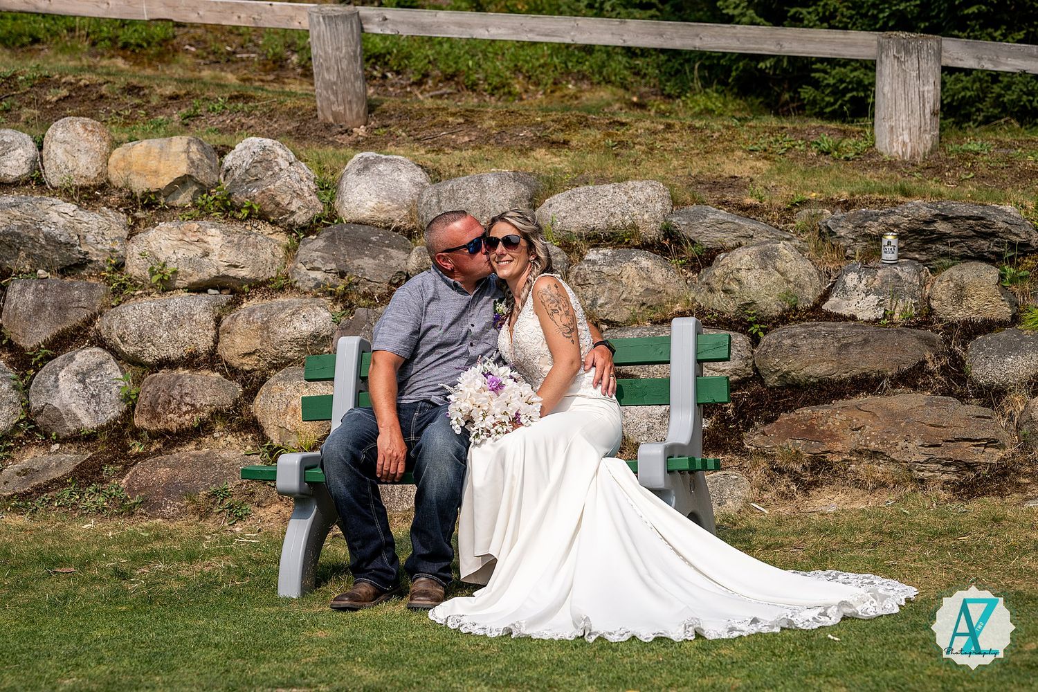 A romantic wedding couple sits on a turquoise bench against an old stone wall in a rustic outdoor setting.