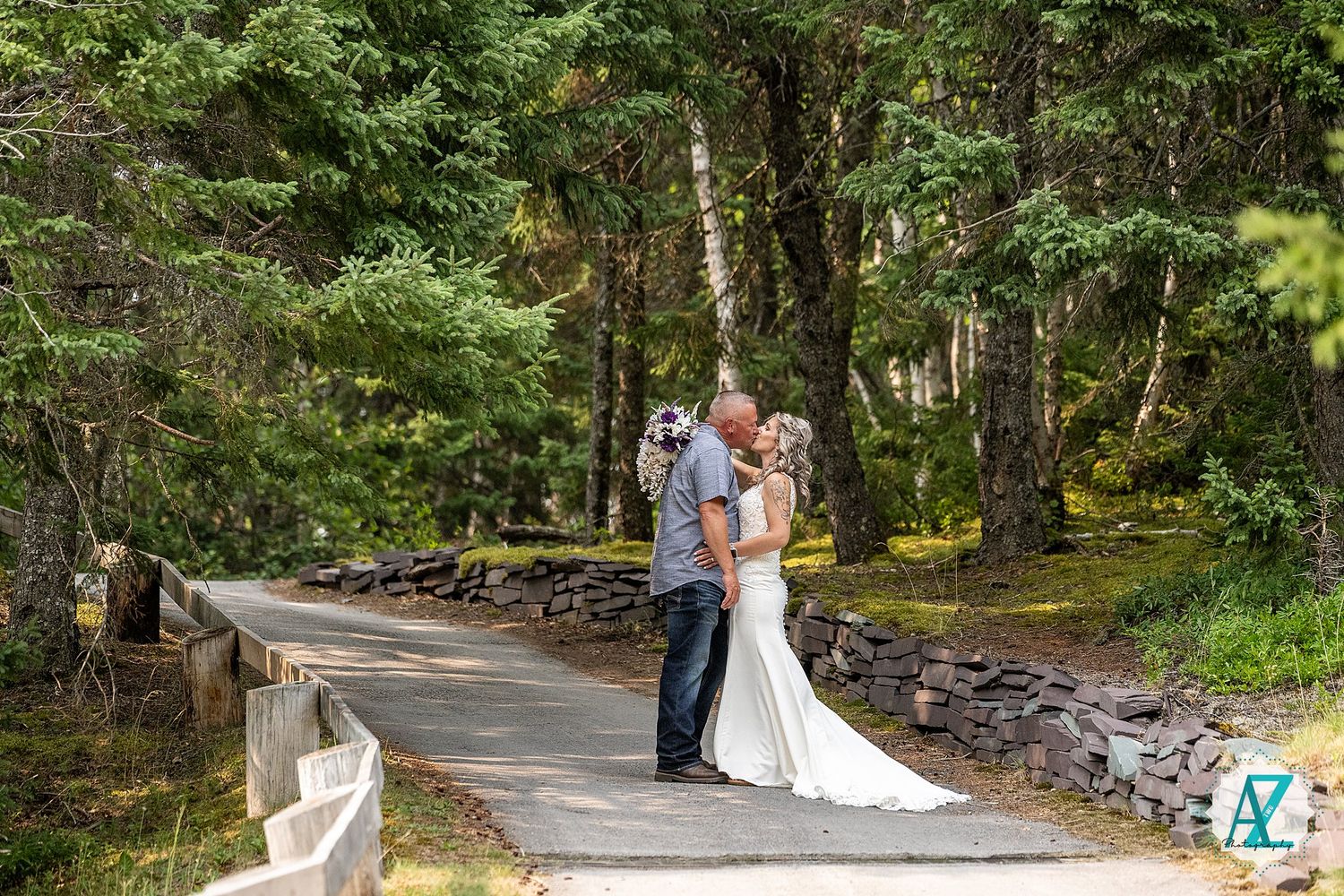 A wedding couple embraces on a tree-lined stone path in a romantic outdoor garden setting.