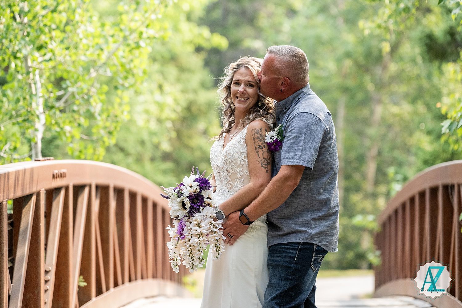A romantic moment shared between a couple on a wooden bridge surrounded by lush greenery and natural light.