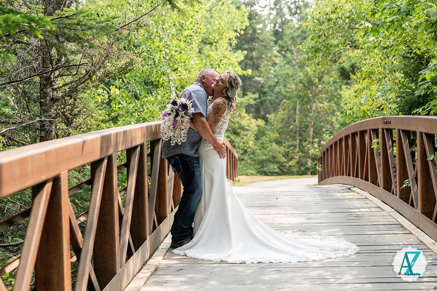 A couple embraces in an intimate pose on a wooden bridge surrounded by lush greenery on their wedding day.