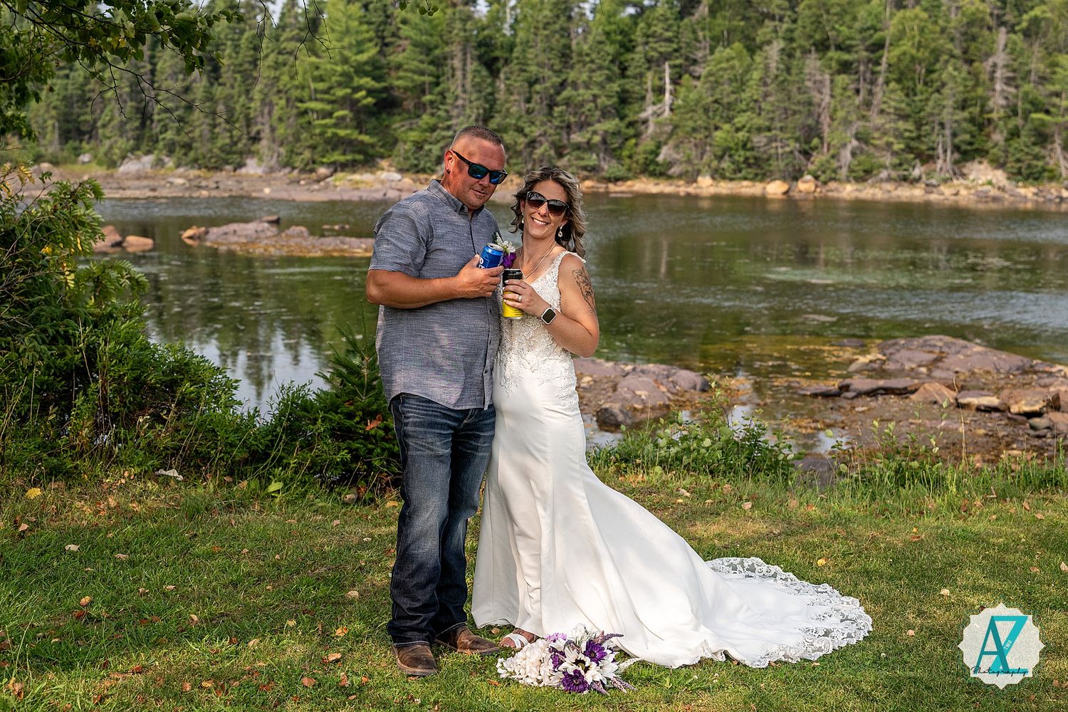 A couple celebrates their outdoor wedding ceremony beside a serene lake surrounded by evergreen trees and rocky shores.