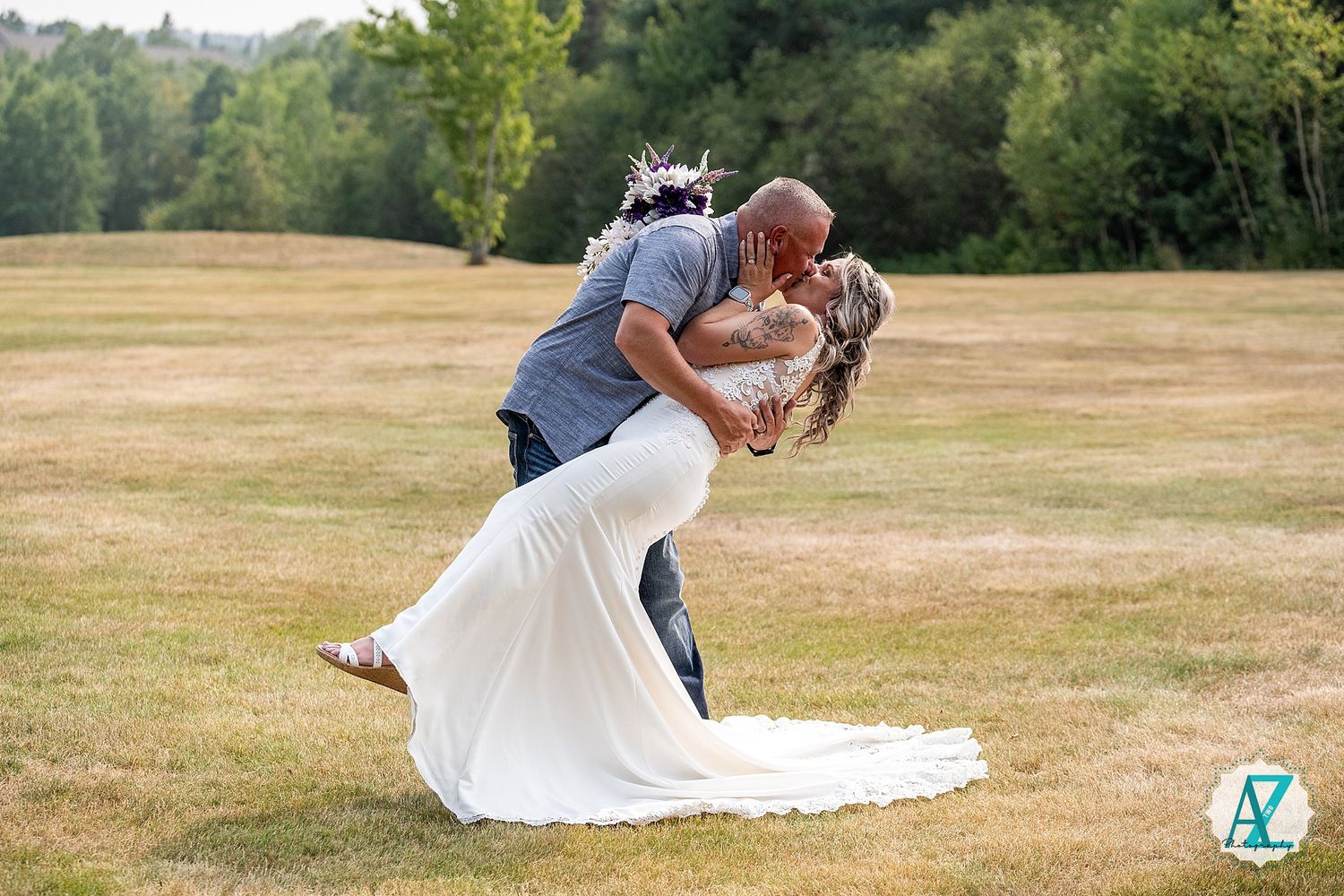 A romantic outdoor wedding moment with a dip kiss in a sunlit grassy field.