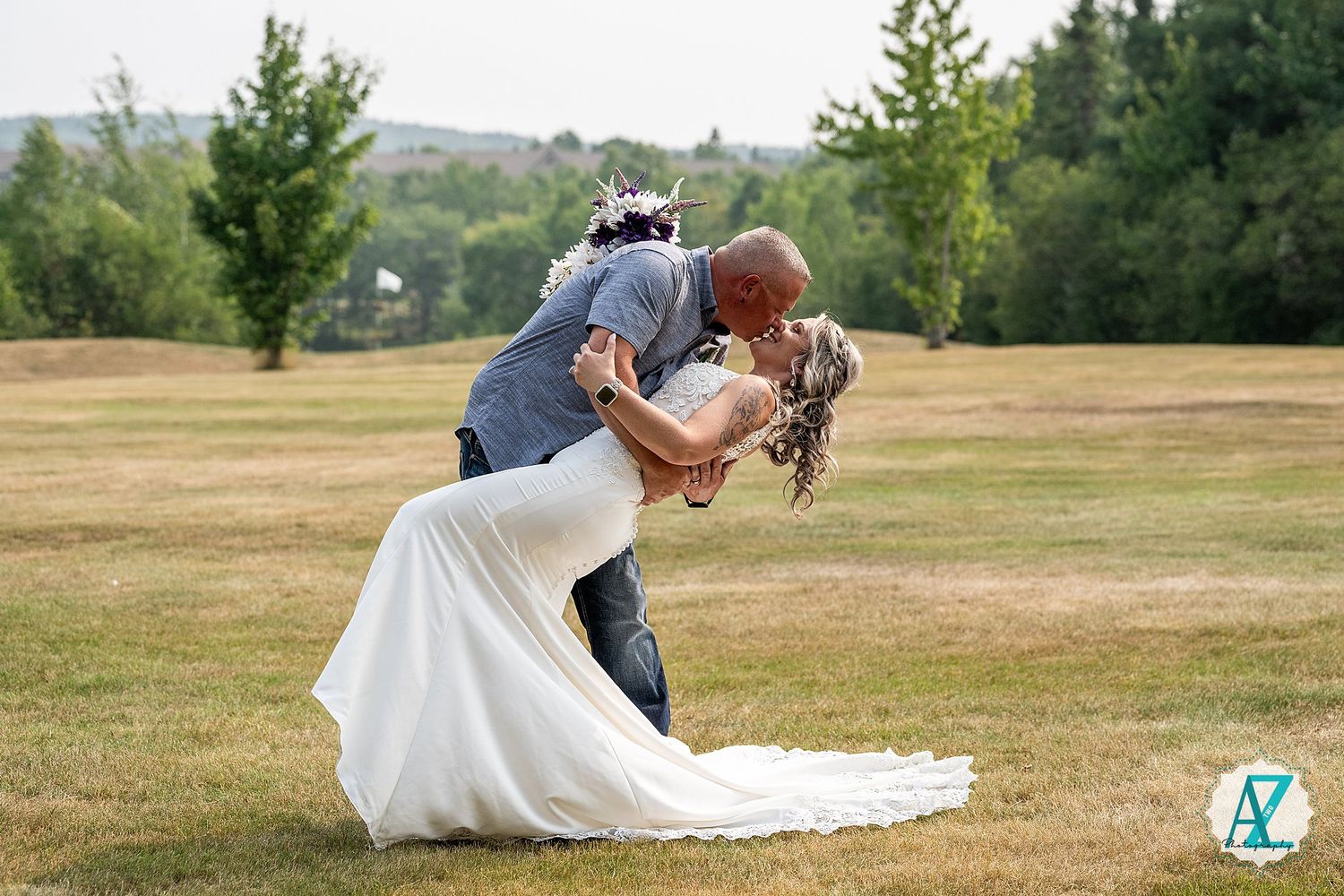 Romantic couple in wedding attire sharing a creative dip pose in a golden field during sunset.