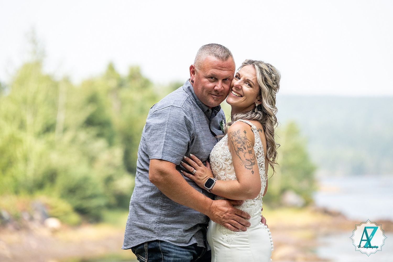 A couple embraces in an intimate outdoor wedding photo with mountains and water in the background.