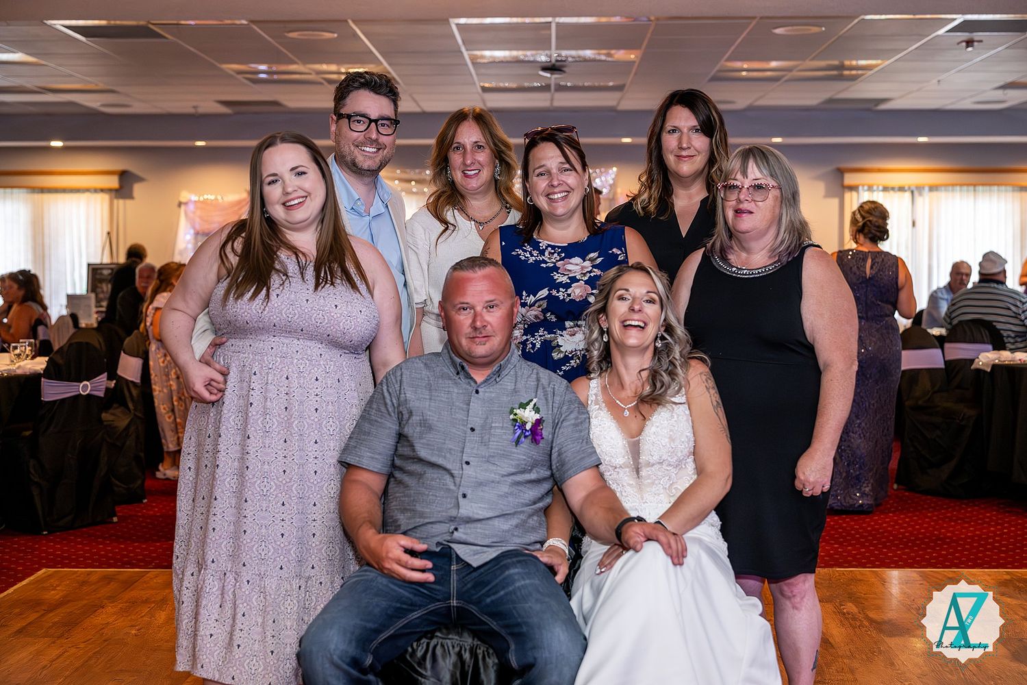 A group celebrates at a wedding reception venue with dance floor and red carpeting in view.