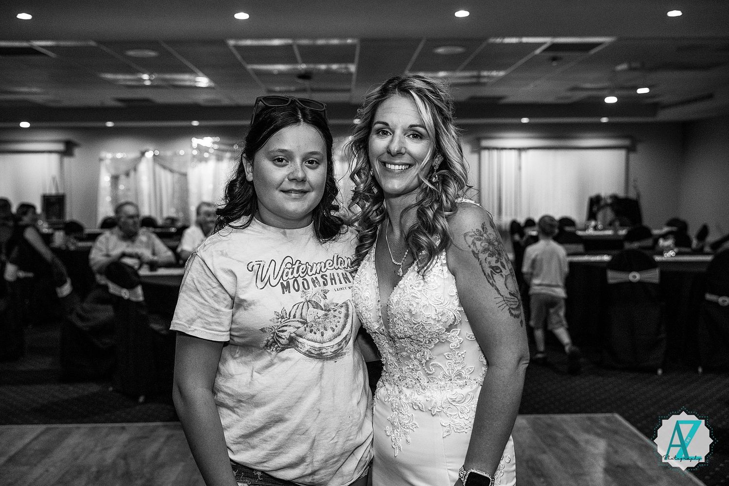 Two women smile together at a casual indoor event wearing matching white outfits.