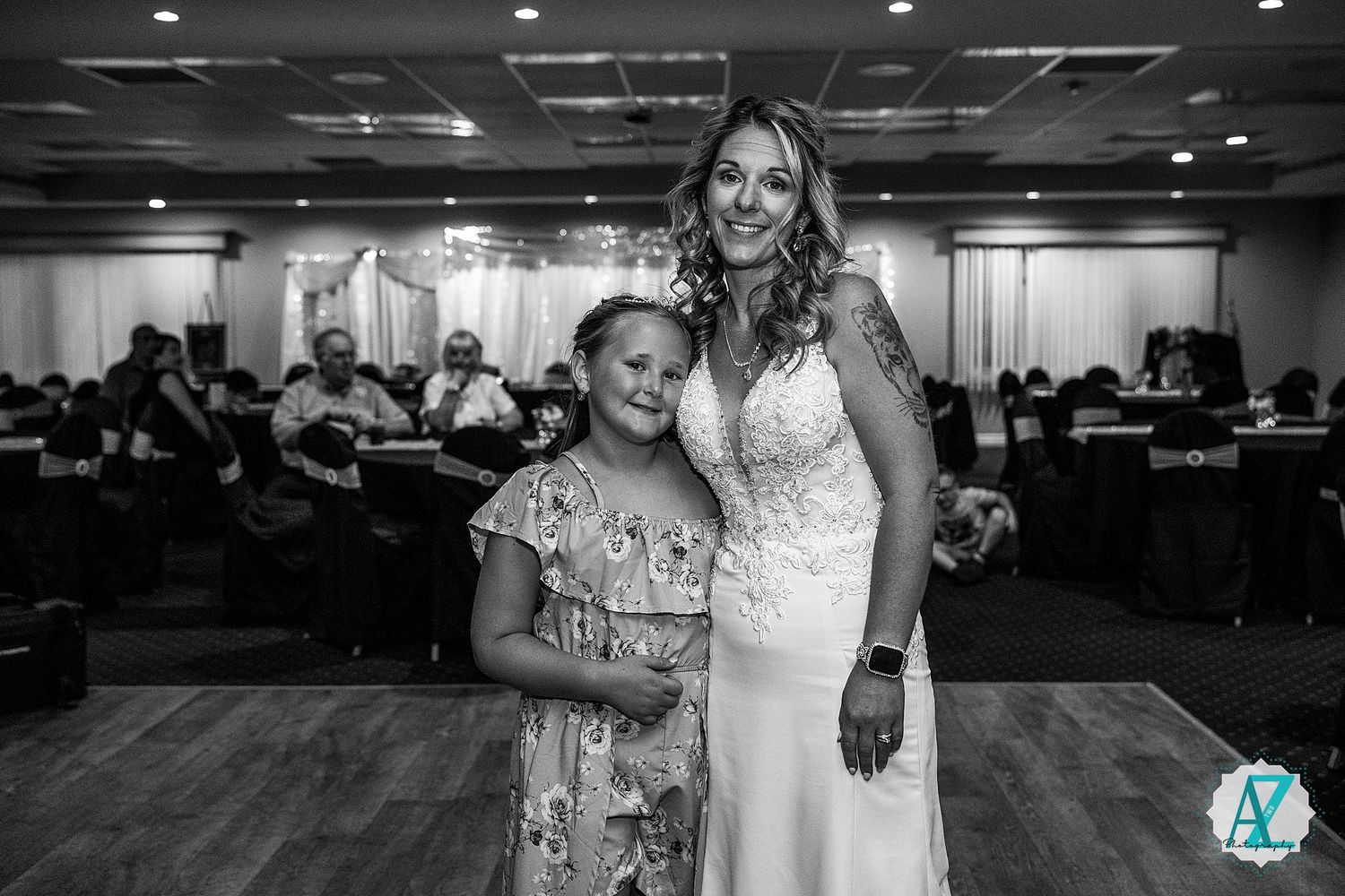 A black and white photograph of a bride and young girl standing together at a wedding reception.