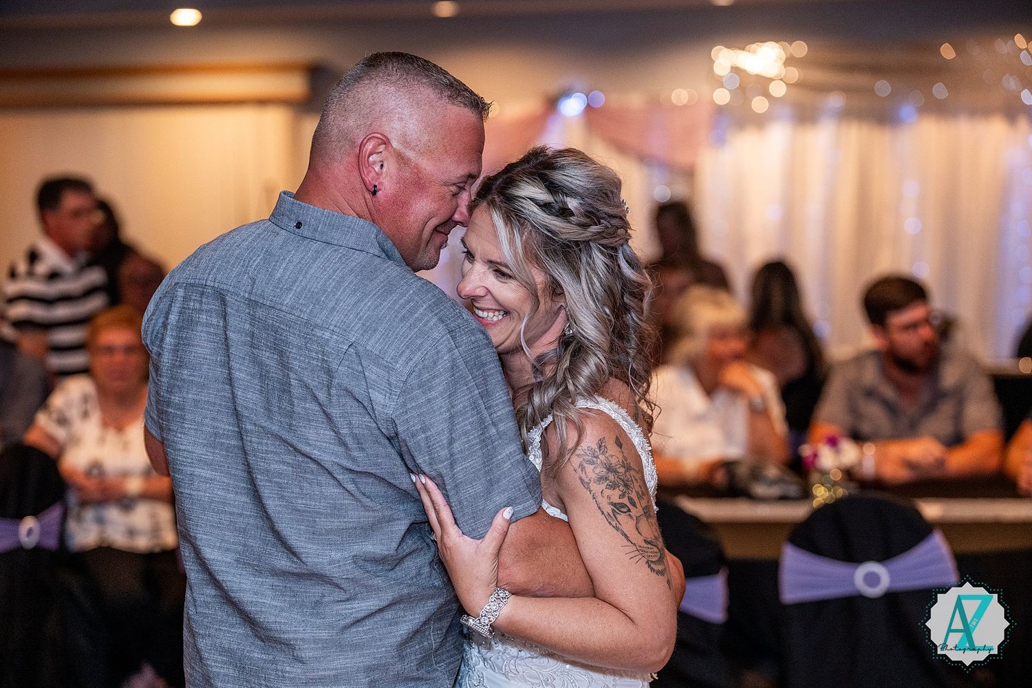 A couple shares an intimate dance moment at their wedding reception while guests watch in the background.