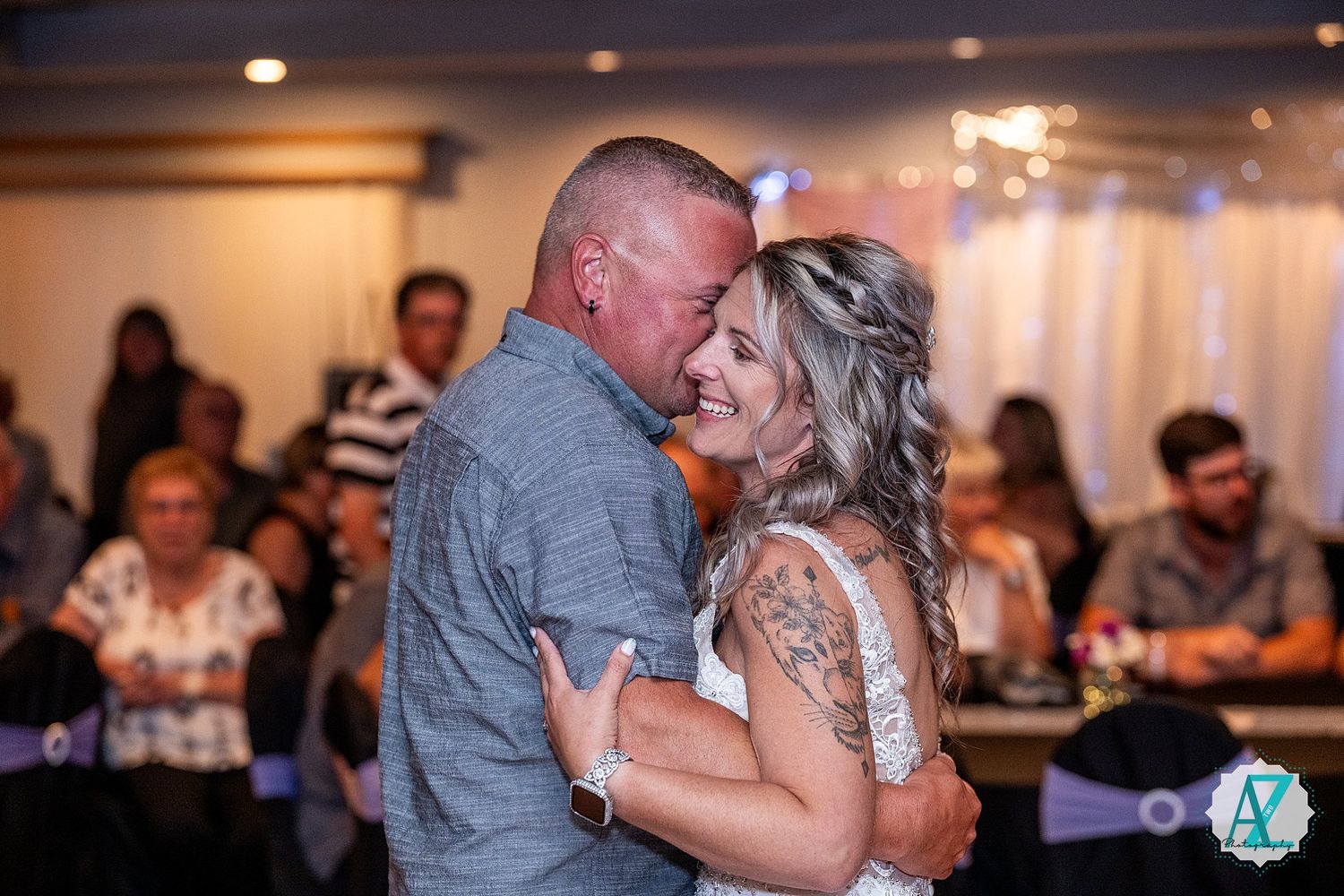 A romantic moment shared during a wedding reception dance with guests watching in the background.