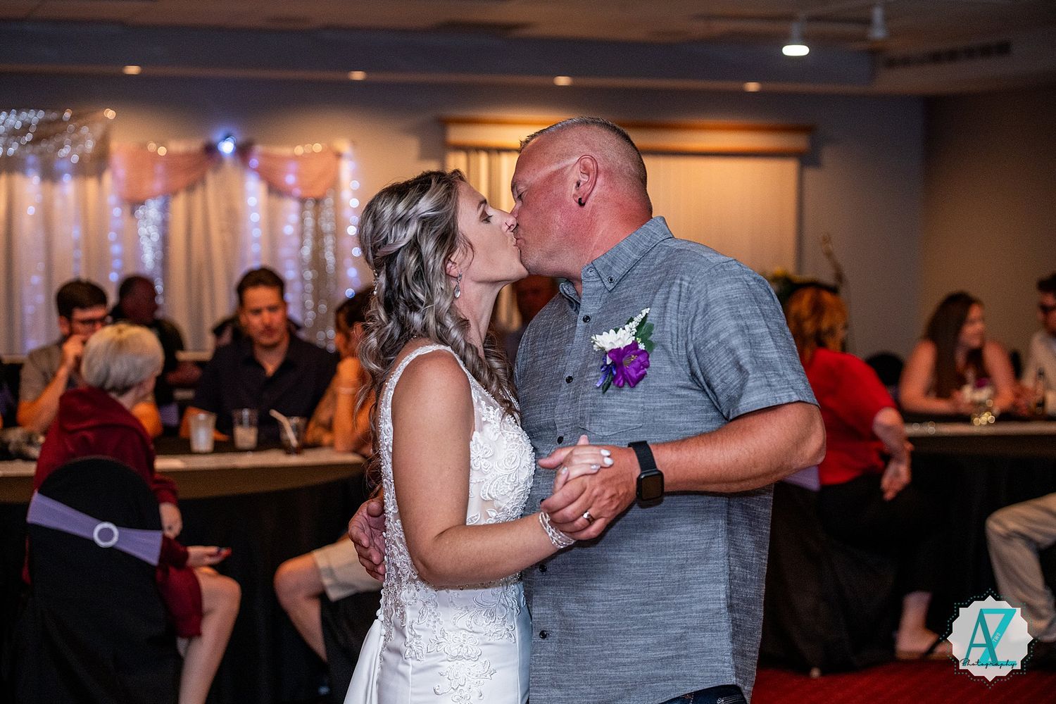 A couple shares their first dance as newlyweds in a reception hall with soft lighting and guests in the background.