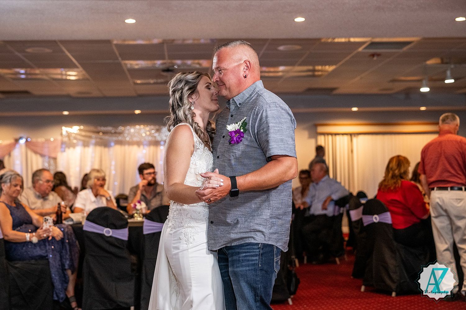 A couple shares their first dance together at a wedding reception in a ballroom decorated with purple accents.