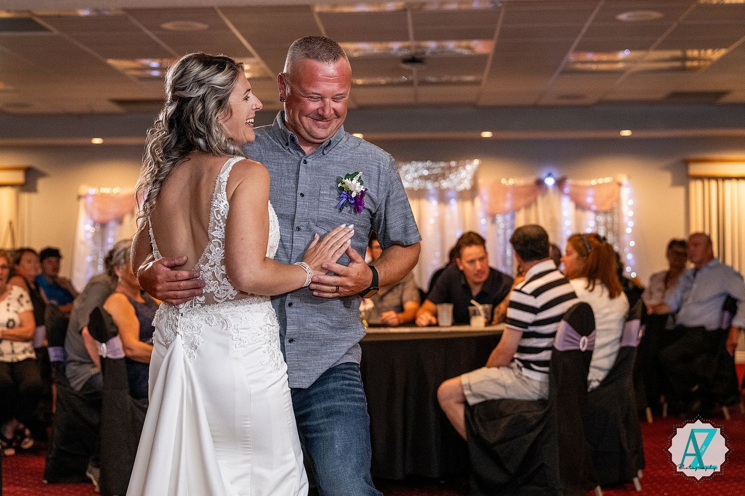 A couple shares a joyful dance moment at a wedding reception in a warmly lit indoor venue.