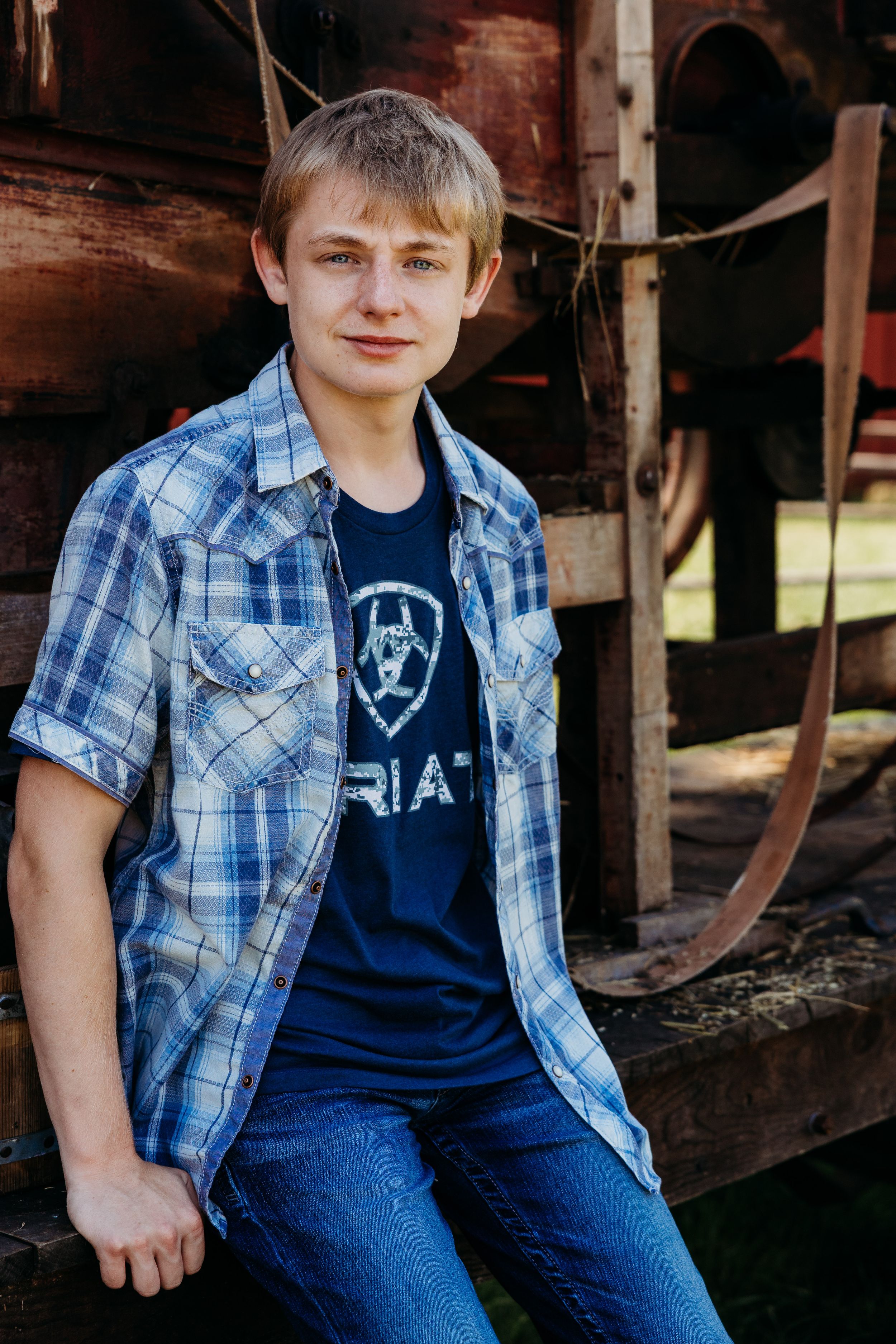 Someone wearing a blue plaid shirt and jeans sits casually on wooden steps in a rustic setting.