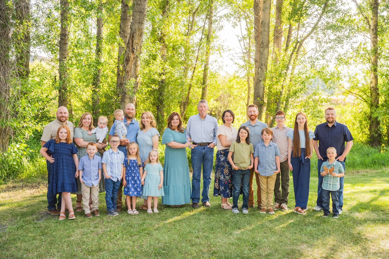 A large group in coordinated blue and white outfits poses together for a portrait in a sunny wooded outdoor setting.