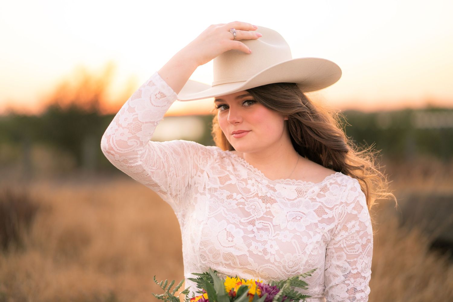 Western bridal portrait with sunflower bouquet and cowboy hat at sunset.