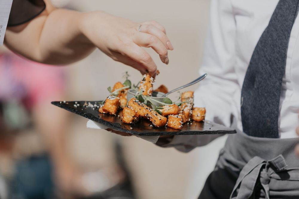 Catering staff plating elegant appetizers with garnish on a dark slate serving plate at wedding.