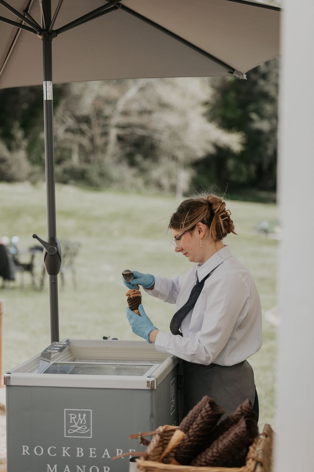 Staff member at Rockbeare Manor preparing ice cream cones at an outdoor wedding reception stand.