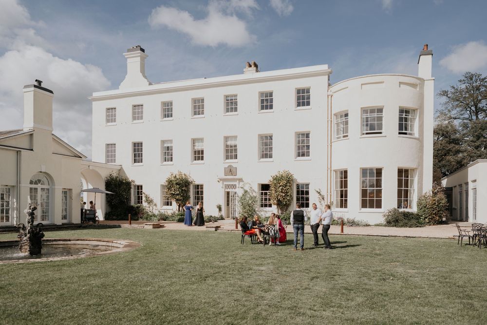 Elegant white Georgian manor house wedding venue with guests gathered on the lawn.