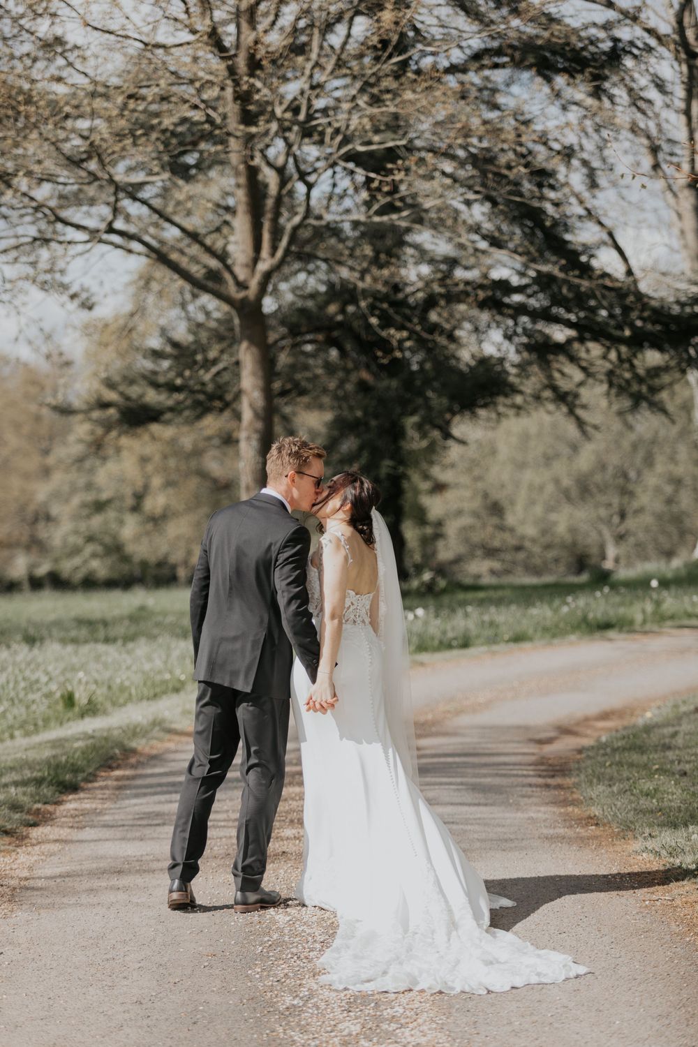 Bride and groom sharing a kiss on a tree-lined path in a romantic outdoor wedding portrait.