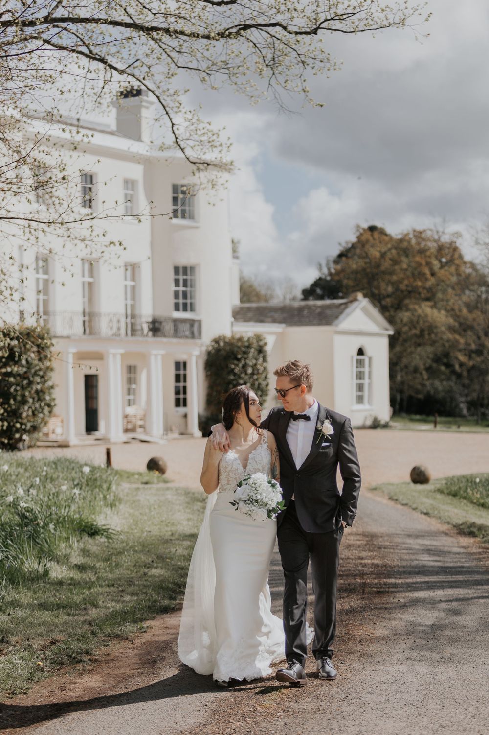 Bride and groom sharing an intimate moment on a driveway outside a grand white manor house.