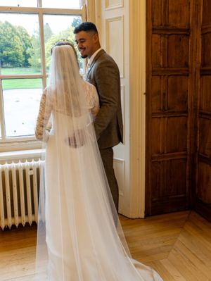 A wedding couple shares intimate moments in an elegant room with wooden floors and large windows.