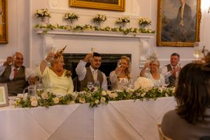 Wedding reception guests seated at elegant tables in an ornate white room with gold framed paintings on the walls.