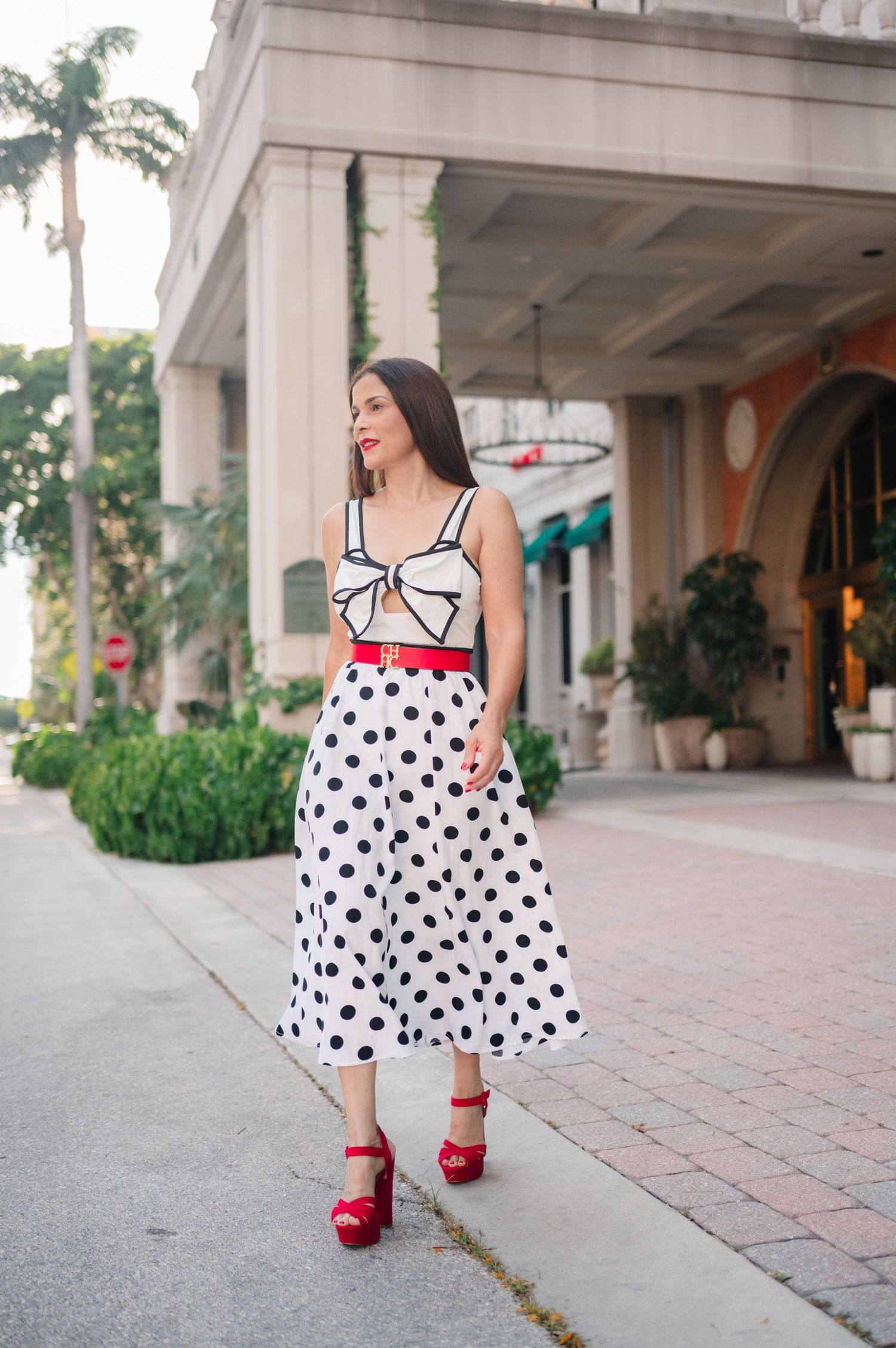 Stylish polka dot midi skirt paired with white bow top and red platform sandals for a retro-inspired summer look.
