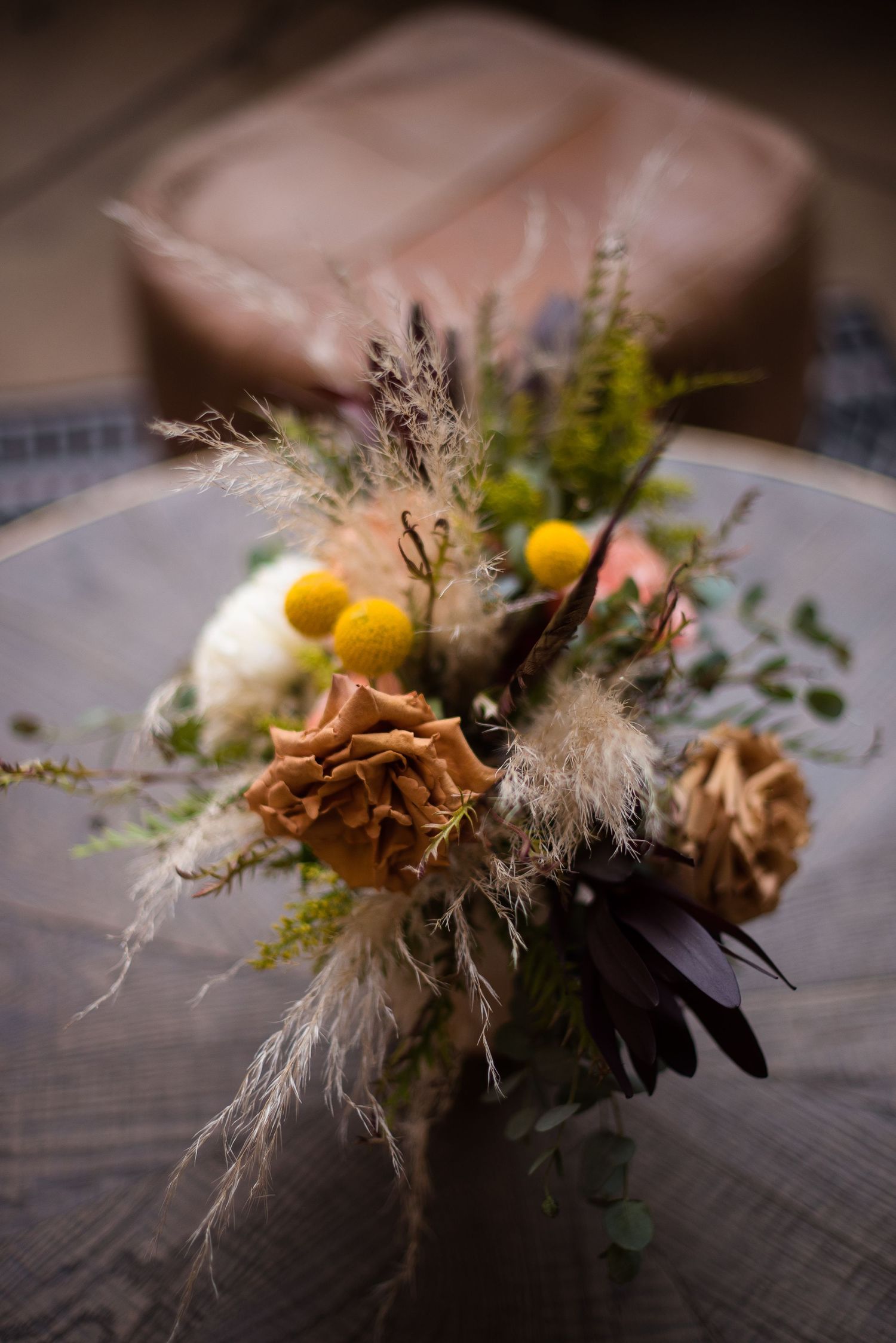 A rustic floral arrangement with dried flowers, yellow berries and natural elements on a wooden surface.