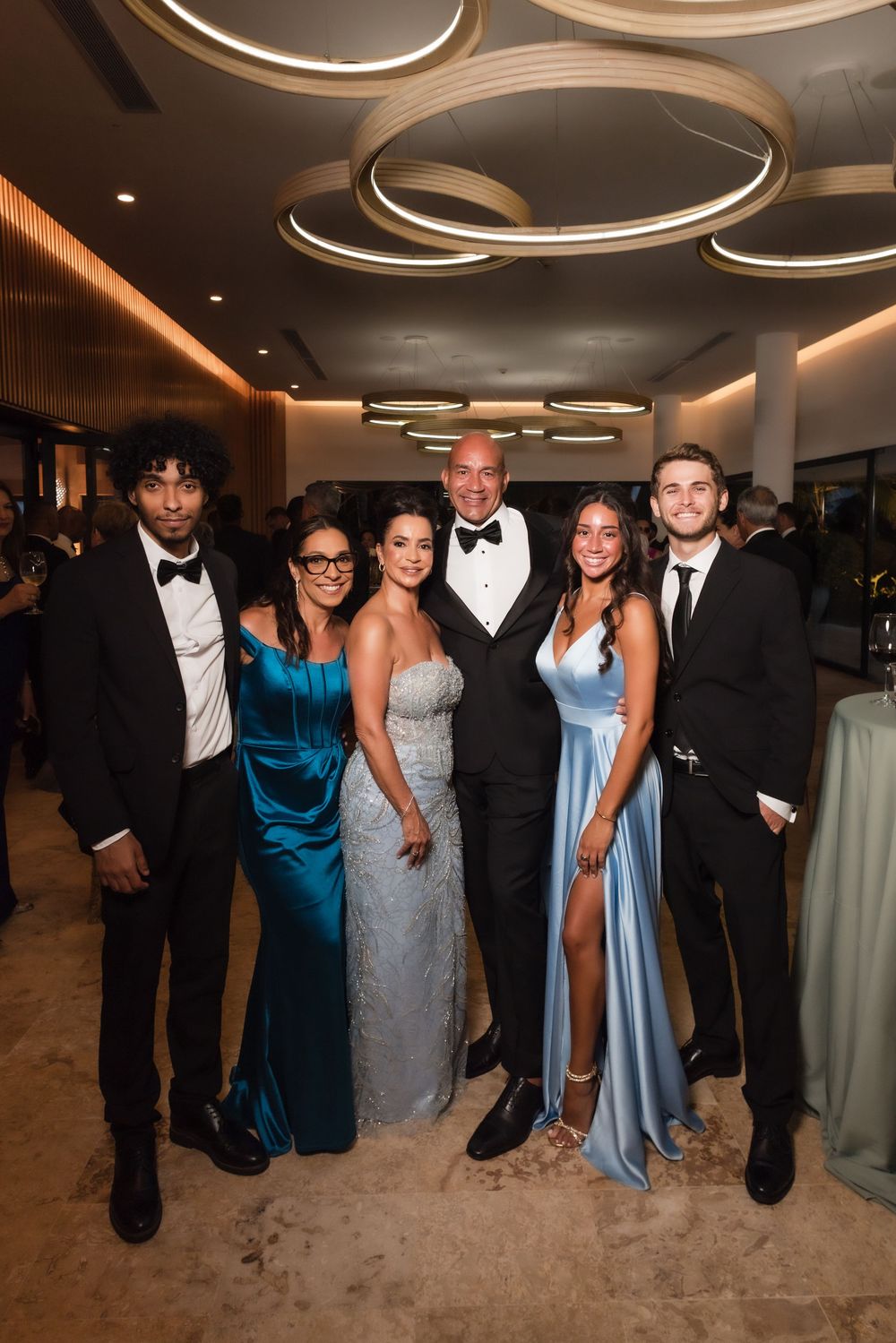 A group poses together at a formal event wearing elegant dresses and tuxedos in shades of blue and black.