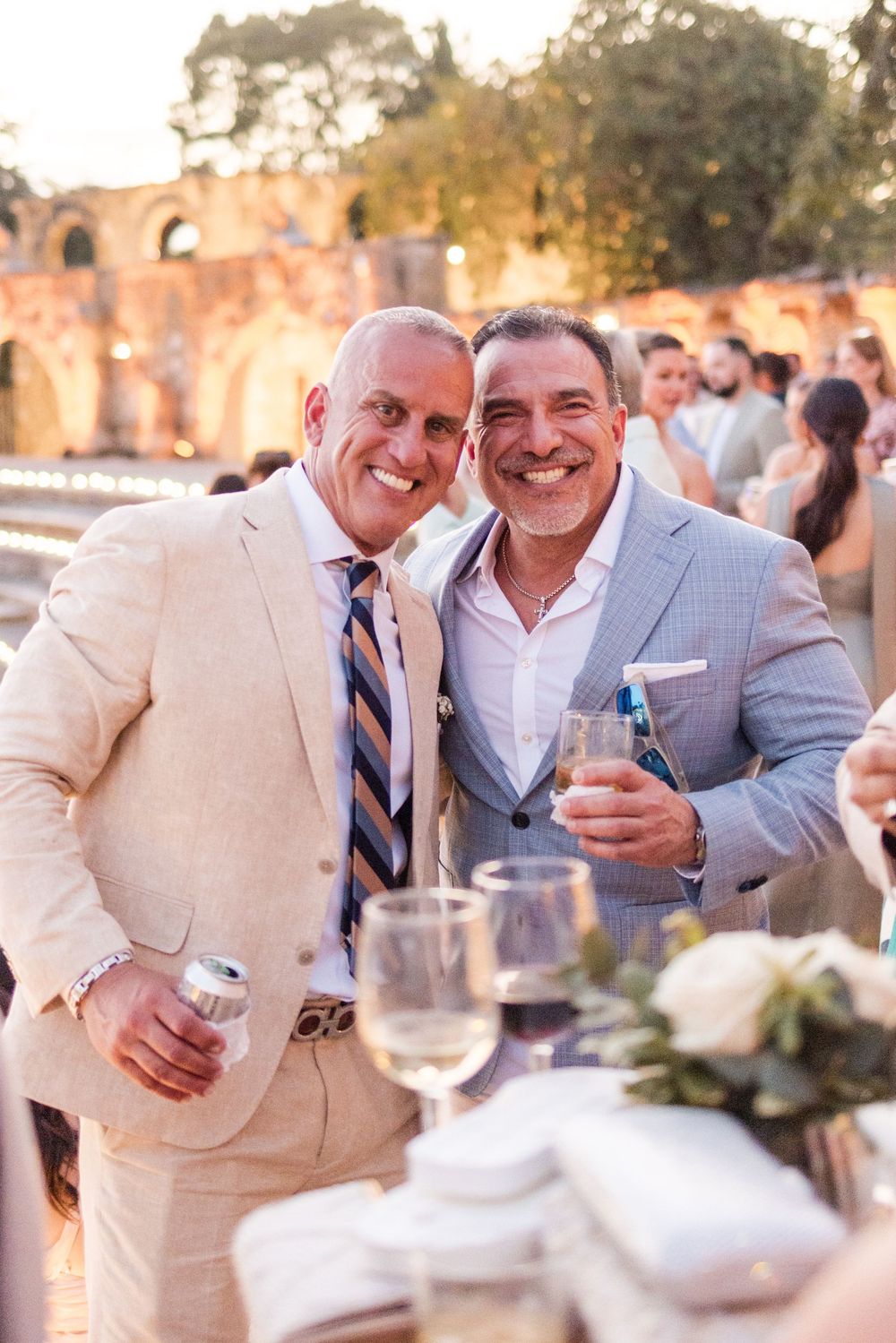 Two people in formal attire share a joyful moment at an outdoor reception with table settings visible in the foreground.