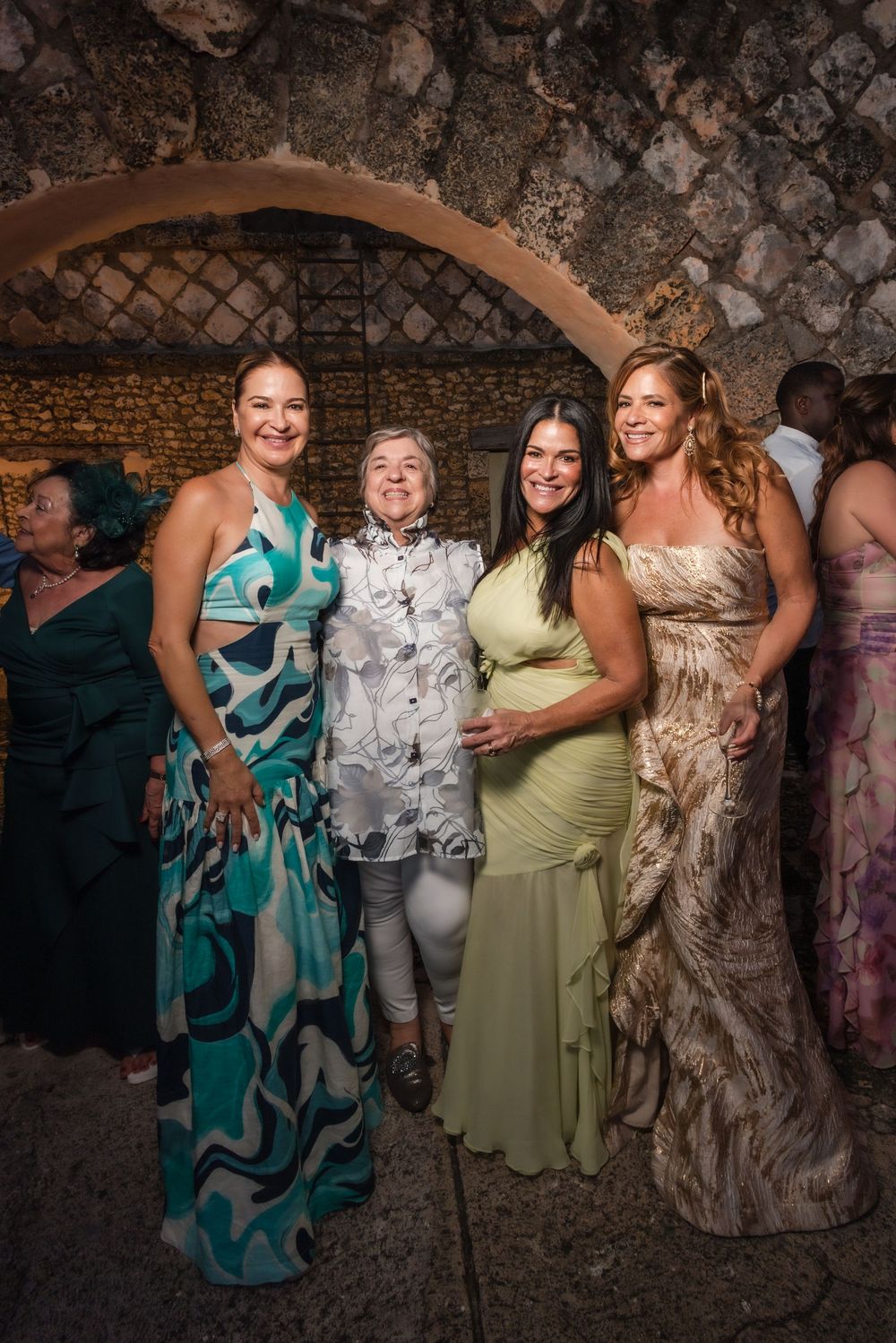 Wedding celebration in a rustic stone venue with guests wearing colorful formal dresses.