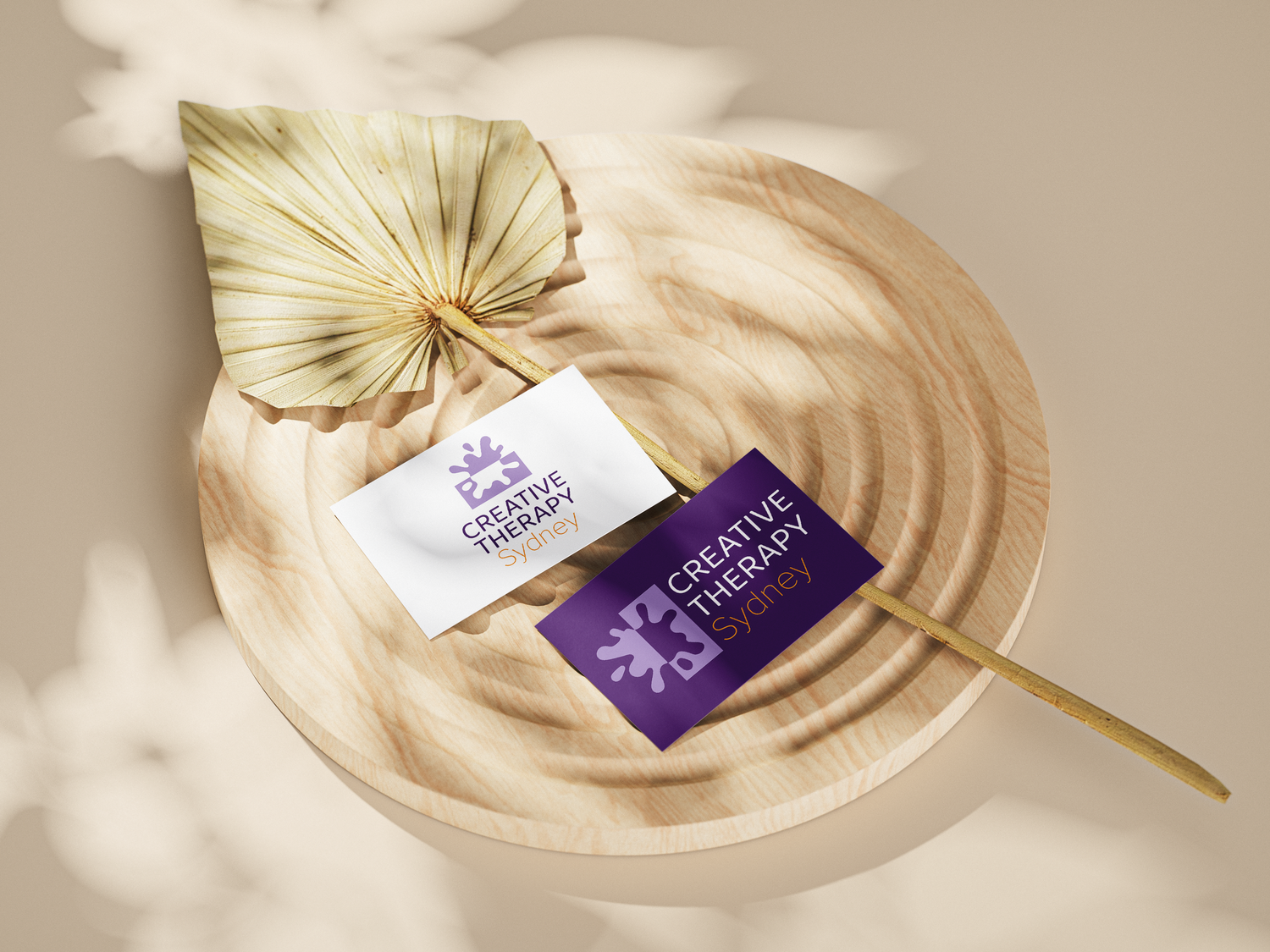 Gold palm leaf with purple business cards displayed on beige surface in elegant minimalist composition.