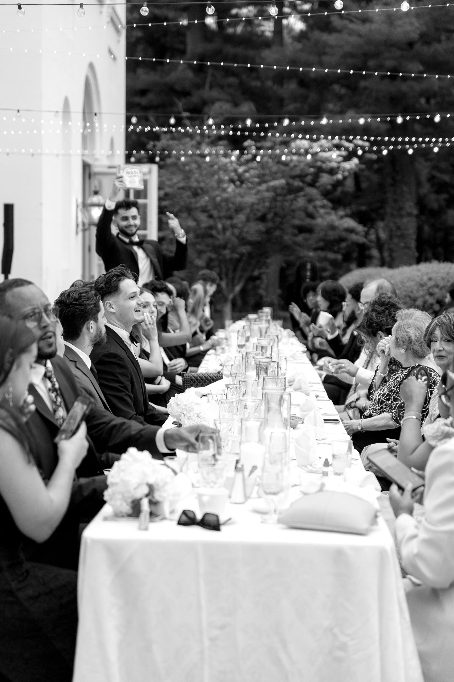 Wedding guests seated at elegant outdoor reception tables with string lights overhead creating a romantic ambiance.