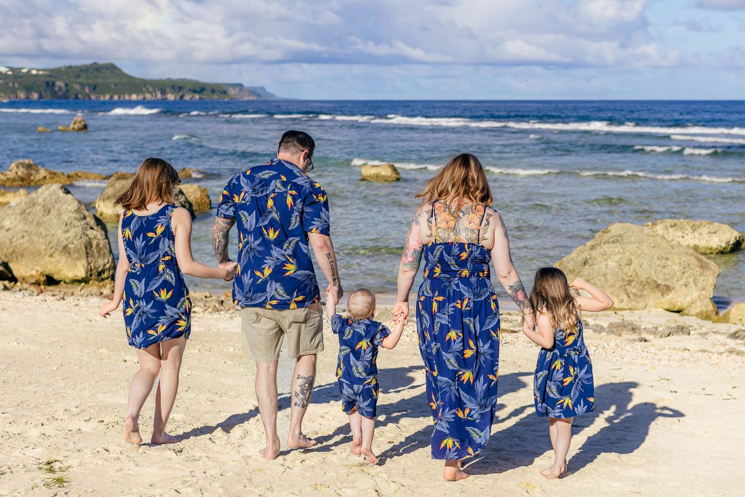Family wearing matching blue outfits walking along a rocky beach shoreline.